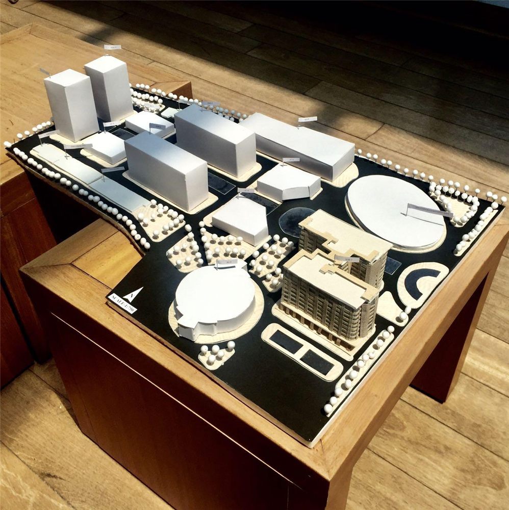 A white card scale model of a campus site plan on a wooden table
